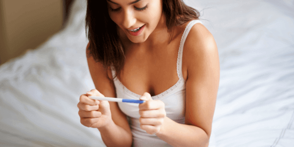 Szczęśliwa kobieta patrząca na pozytywny test ciążowy