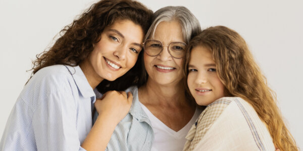 Trzy pokolenia uśmiechniętych kobiet – babcia, mama i córka – obejmują się, symbolizując troskę o zdrowie i profilaktykę raka szyjki macicy