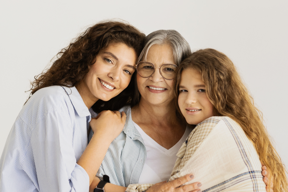 Trzy pokolenia uśmiechniętych kobiet – babcia, mama i córka – obejmują się, symbolizując troskę o zdrowie i profilaktykę raka szyjki macicy