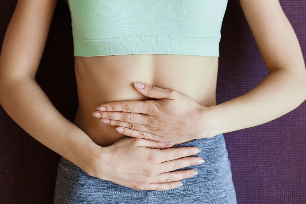 Kobieta trzymająca dłonie na brzuchu odczuwając objawy przedwczesnej menopauzy